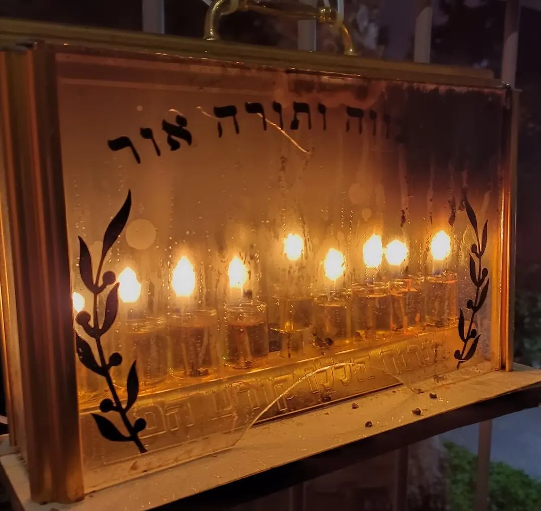 Hannukah menorah in glass case, eight candles and shamash are lit.
