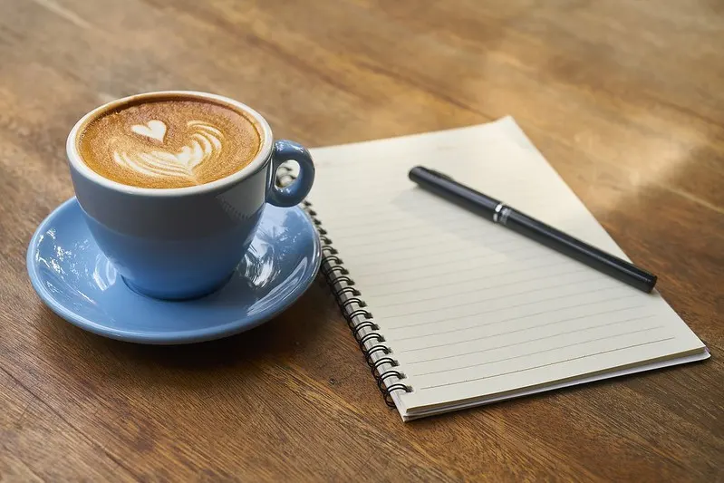 cappuccino in a blue demitasse next to a blank spiral-bound notebook with
closed pen resting on top